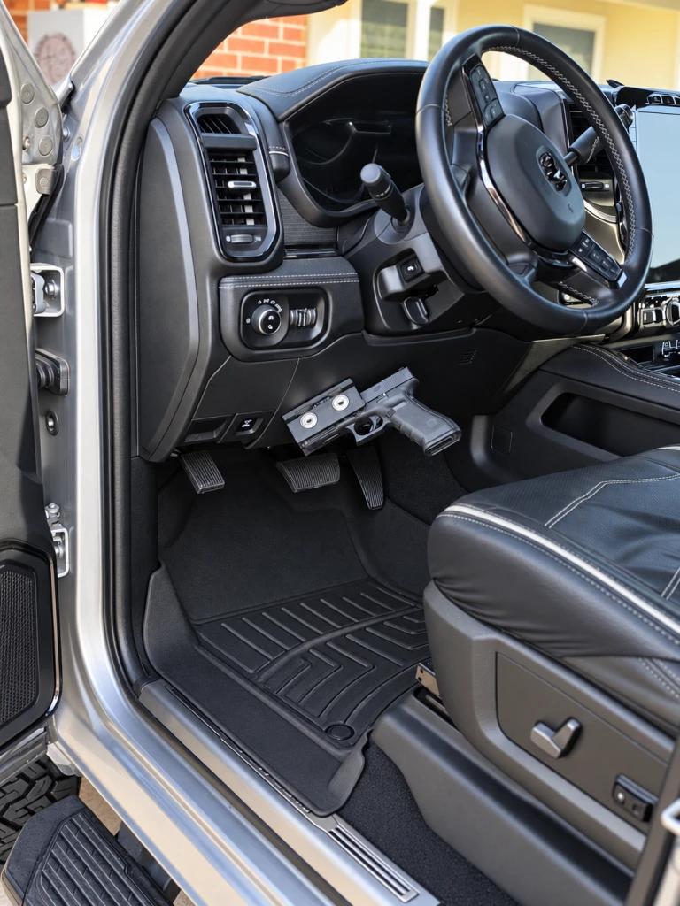 Pistol held in an At The Ready mount on the lower dash panel of a pickup truck, beside the pedals